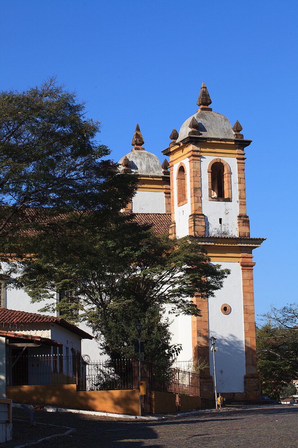 Igreja de Nossa Senhora do Carmo, em Sabará, com torres de pedra, árvores e casario histórico